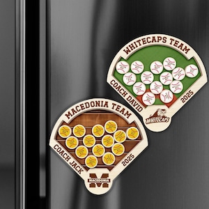 May include: Two wooden baseball-themed magnets. One features a green field with white baseballs and the text "Whitecaps Team" and "Coach David". The other has a brown field with yellow baseballs and the text "Macedonia Team" and "Coach Jack". Both have the year 2025.