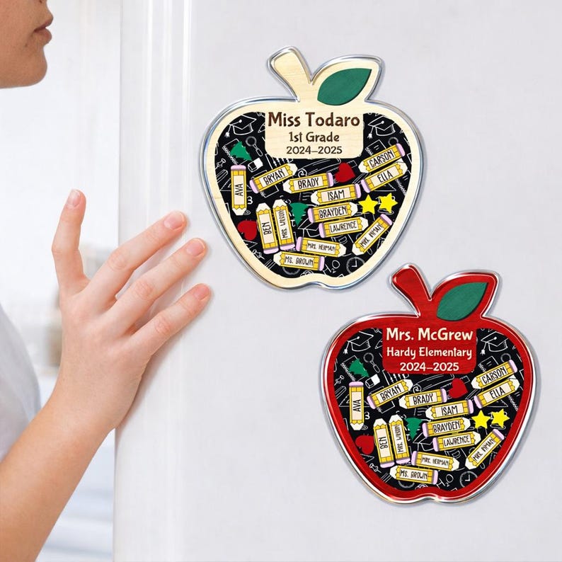 May include: Two apple-shaped magnets. One is red, the other is natural wood. Both have a black background with school-themed icons and student names. The wooden apple says "Miss Todaro 1st Grade 2024-2025". The red apple says "Mrs. McGrew Hardy Elementary 2024-2025".