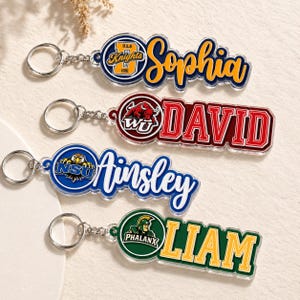 May include: Four personalized keychains with names and university logos. The keychains feature the names Sophia, David, Ainsley, and Liam in various fonts and colors. Each keychain has a silver keyring and chain.