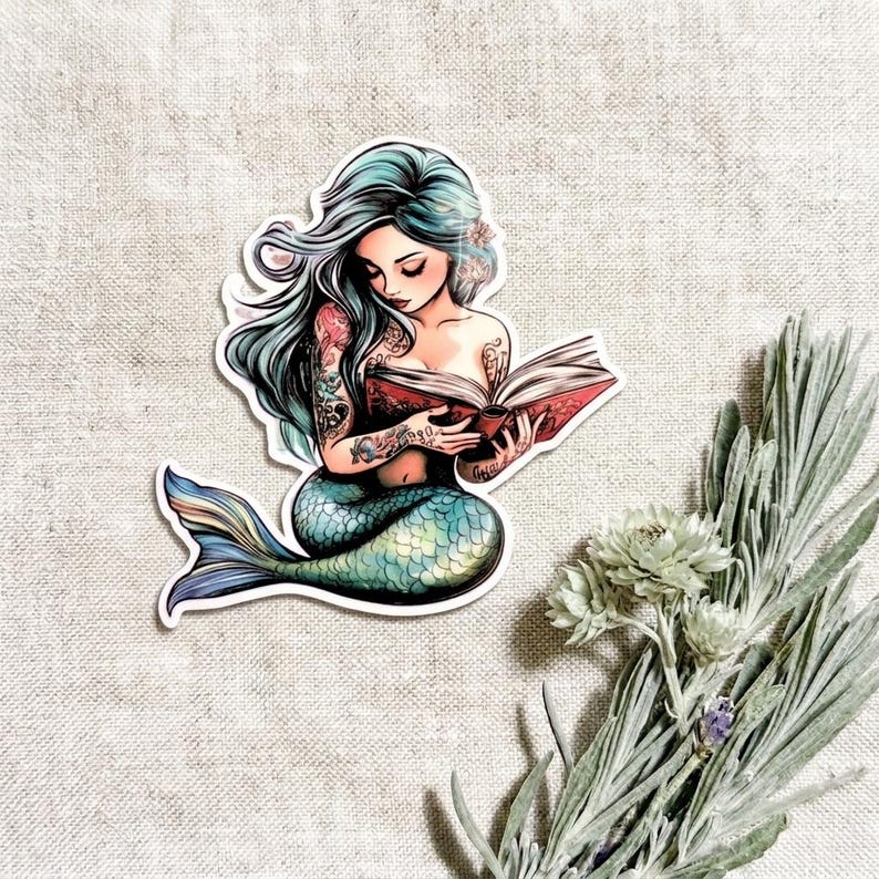 Close-up of a single teal mermaid vinyl sticker on a linen background with dried lavender flowers. The mermaid has long silver-green hair and a shimmering blue-green tail, absorbed in reading an open book.