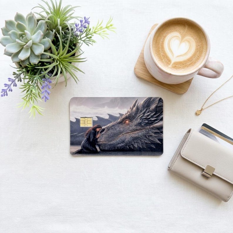 a debit card skin of a black dragon laying it's head down so a human can rest her head on the dragon on a cream colored cloth,  and a wallet 
flower and a hot coffee
 made by thestickerera