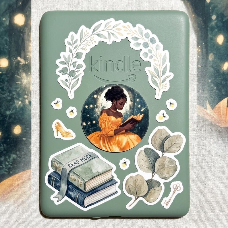 Sage green Kindle case decorated with vinyl stickers, including a white botanical wreath framing the logo, a Black woman in a yellow gown reading inside a glowing moon, a glass slipper, a stack of blue books with a Read More ribbon, a small key, eucalyptus leaves, and fireflies on a dreamy fairytale background.