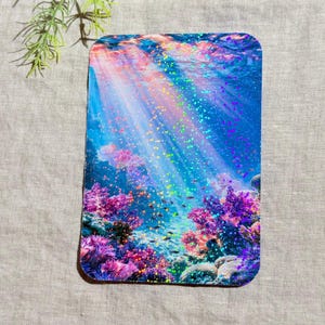 May include: A rectangular sticker featuring a vibrant underwater scene with bright pink and purple coral reefs at the bottom. Sunlight rays filter through the deep blue water from above, overlaid with a shimmering holographic glitter effect.