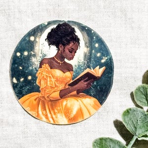 Vinyl sticker of a Black woman in a flowing yellow off-shoulder gown reading a book inside a glowing circular moon, surrounded by fireflies, set against a linen background with green eucalyptus leaves.