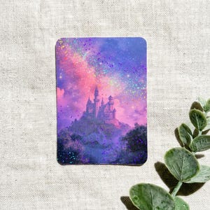 May include: A rectangular card featuring a holographic print of a castle silhouette set against a vibrant nebula background of pink, purple, and blue hues, with scattered sparkling light effects across the entire surface of the image.