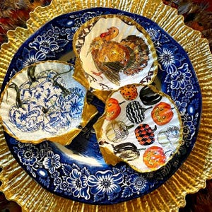 May include: Four decorative plates with gold trim, each featuring a different design. One plate has a blue and white floral pattern, another has a turkey, another has pumpkins and spiders, and the last has a black and white pattern.