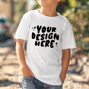 Może przedstawiać: Biała koszulka z czarnym napisem "YOUR DESIGN HERE" z małymi gwiazdkami po obu stronach napisu.
