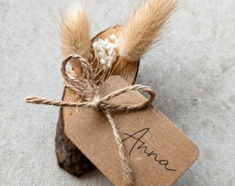 Tarjeta de mesa para boda de estilo bohemio con flores secas y una pequeña rodaja de árbol con la tarjeta del nombre: un pequeño recuerdo para los invitados.