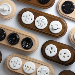 Könnte beinhalten: Eine Sammlung von elektrischen Wandplatten mit verschiedenen Konfigurationen von Schaltern, Steckdosen und USB-Anschlüssen. Die Platten sind aus Holz gefertigt und haben weiße und schwarze Komponenten. Die Designs reichen von einfachen Kippschaltern bis zu komplexeren Anordnungen.