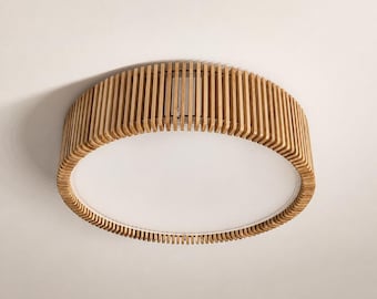 May include: A circular flush mount ceiling light fixture featuring a light brown wooden slat frame surrounding a flat, white, circular diffuser panel. The wooden slats are arranged vertically in a continuous ring around the central light source.