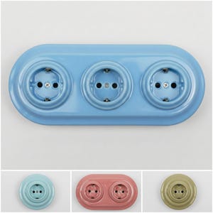 Puede incluir: Una placa de enchufe eléctrica ovalada azul claro con tres enchufes circulares. Cada enchufe tiene dos agujeros y un pasador de conexión a tierra. La placa está montada sobre una superficie blanca. Imágenes adicionales muestran placas de enchufe individuales y dobles.