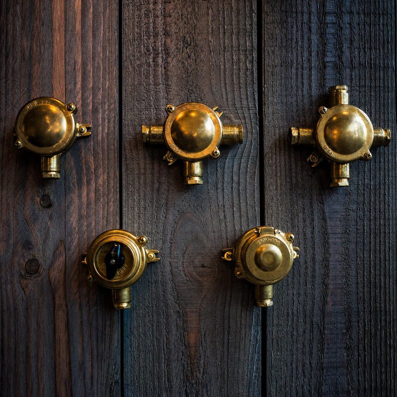 May include: Five antique brass electrical junction boxes and switches are mounted on a dark wood surface. The boxes have a circular design with various outlet configurations. The brass has a warm, aged patina.