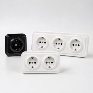 Può includere: Una collezione di prese elettriche a muro composta da una presa singola quadrata nera, una presa doppia rettangolare bianca e una presa tripla rettangolare bianca. Ogni unità presenta una finitura liscia e lucida con fori circolari.
