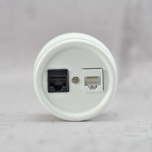 May include: A circular white wall plate featuring two modular ports. One port is black and the other is white, positioned side-by-side. A small silver metal screw is located in the center between the two ports, securing the faceplate in place.