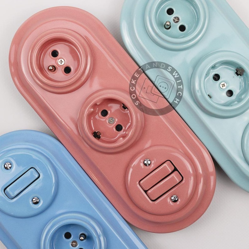 May include: Three ceramic electrical wall plates in pastel pink, light blue, and mint green. The pink plate features two circular outlets and one toggle switch. The blue and green plates feature circular outlets and toggle switches.