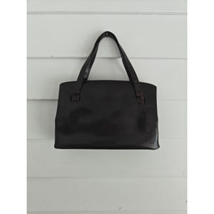 May include: A black leather tote bag with two handles. The bag has a rectangular shape with rounded corners and a smooth, glossy finish. The handles are attached with small, square-shaped connectors.