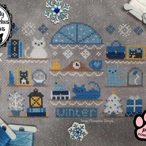 May include: Cross-stitch pattern featuring a winter scene with cats, books, and a Christmas tree. The design includes the text "WINTER" and the logo "Simply Meowvelous Designs". The color palette includes blue, white, and yellow.