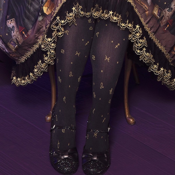 May include: Black tights featuring a gold-toned zodiac symbol and star pattern, paired with black glittery Mary Jane shoes with a bow detail. The tights are worn under a black skirt with a gold star-patterned lace trim hem.