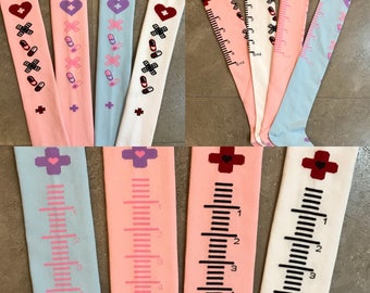 Può includere: Quattro paia di calze alte al ginocchio con diversi design. Due paia sono rosa con un cuore bianco e una croce con pillole e bende. Un paio è azzurro con un cuore bianco e una croce con pillole e bende. Un paio è bianco con un cuore rosa e una croce con pillole e bende. La parte inferiore di ogni calza ha un righello con segni fino a 5 ml.