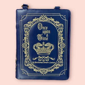 May include: A blue faux leather book clutch with a gold embroidered design. The design features a crown, ornate scrollwork, and the text "Once upon a Time" by Enchanted Dream Couture.