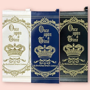 May include: Three different colored zippered pouches with a gold embroidered design. The pouches feature a crown and the text "Once upon a Time" with the words "by Enchanted Dream Couture" at the bottom.
