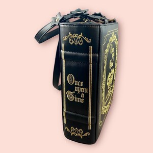May include: Black book-shaped handbag with a gold strap and gold embroidery that reads "Once Upon a Time".