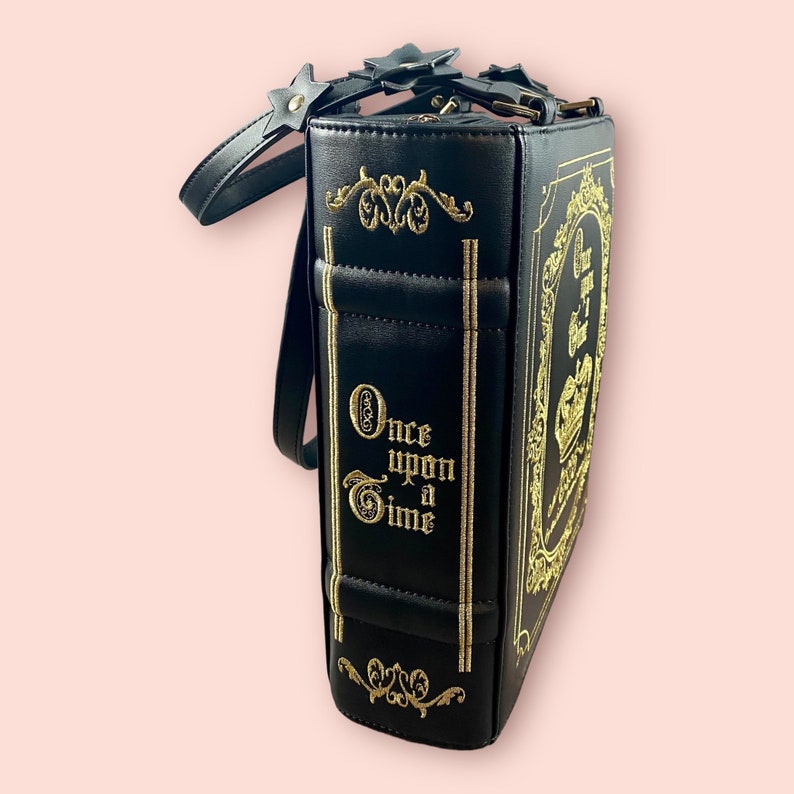 May include: Black book-shaped handbag with a gold strap and gold embroidery that reads "Once Upon a Time".