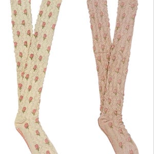 May include: Two pairs of knee-high socks. One pair is cream, the other is pale pink. Both feature a repeating pattern of pink roses and green leaves. The socks have a textured, ruffled appearance.