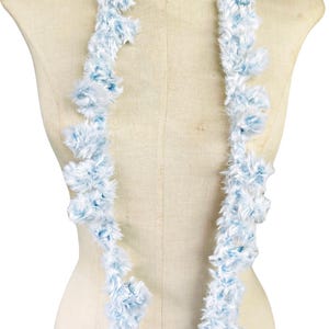May include: A fluffy, light blue and white lei necklace. The lei is made of soft, feathery material and is draped around a mannequin. The lei is a traditional Hawaiian garland, often worn for celebrations.