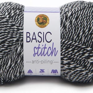 May include: A skein of Basic Stitch yarn in black and white. The yarn is tightly wound and has a textured appearance. The label features the Lion Brand Yarns logo and the words "BASIC stitch" in large letters. The yarn is anti-pilling.