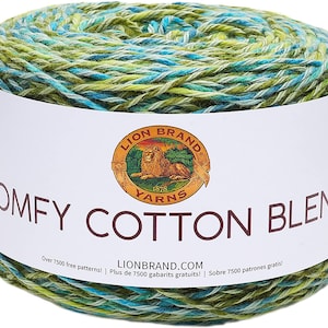 May include: A skein of Lion Brand Comfy Cotton Blend yarn in a green, blue, and white colorway. The label reads "Comfy Cotton Blend" and features the Lion Brand logo with a lion and the words "Lion Brand Yarns 1878". The label also includes the text "Over 7500 free patterns! Plus de 7500 gabarits gratuits! | Sobre 7500 patrones gratis!" and the website address "LionBrand.com".