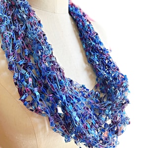 May include: A blue and purple crocheted infinity scarf made of yarn with a shimmery finish.