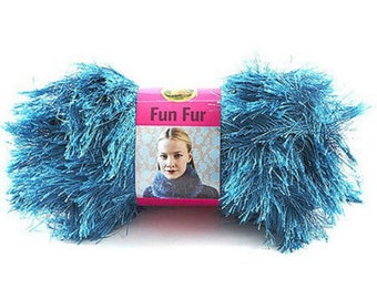 May include: A skein of teal blue Fun Fur yarn. The yarn is a fluffy, fuzzy texture. The label reads "Fun Fur" and features a woman wearing a teal blue scarf.