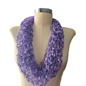 May include: A purple crocheted infinity scarf with a delicate, open-weave design. The scarf is soft and lightweight, making it perfect for layering or wearing on its own.