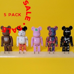 May include: Five pack of collectible bear-shaped figures. The figures are brown, white, pink, blue and black. The figures are all different designs and have various details. The figures are on a white display stand. The text "SALE" is in the top left corner of the image. The text "5 PACK" is in the top center of the image.