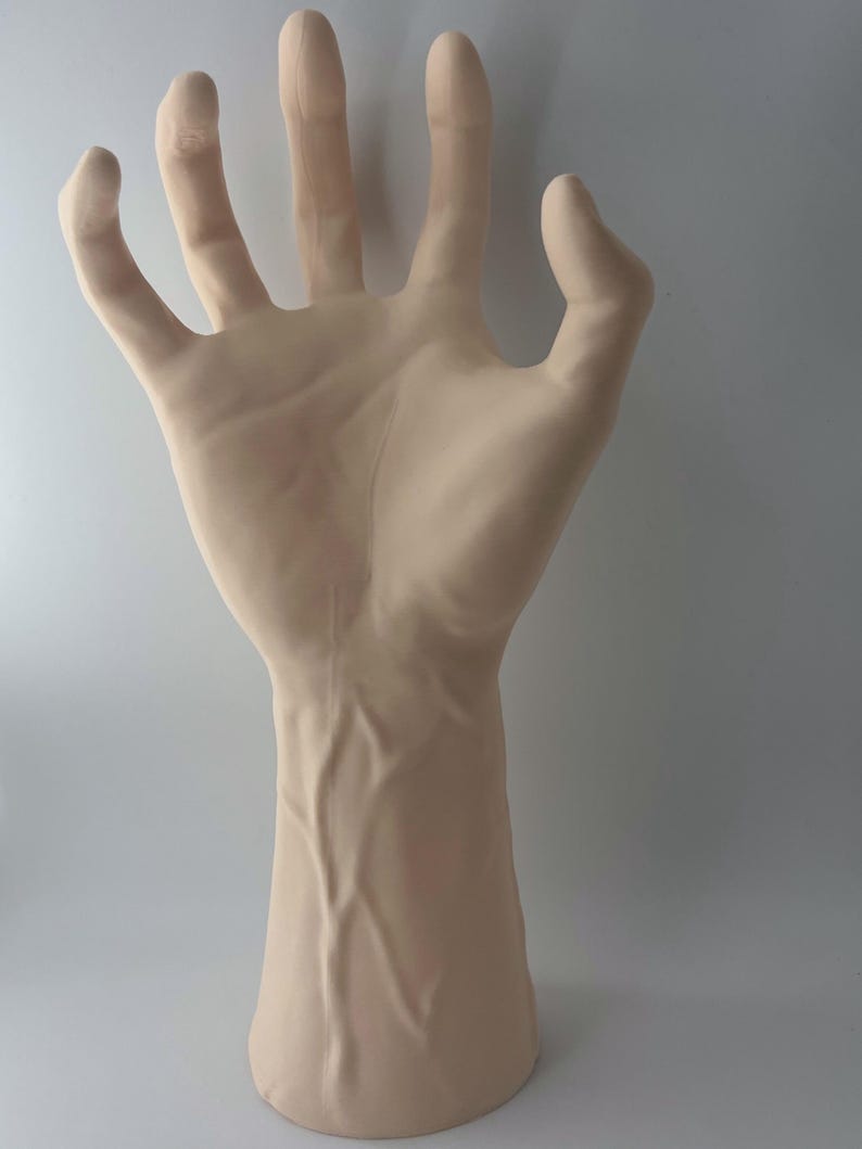 May include: A realistic-looking, pale-toned, sculpted hand with veins, posed with fingers extended and slightly splayed. The hand is attached to a forearm, and the sculpture is made of a smooth, matte material.