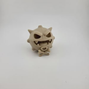 May include: A tan-colored, cartoonish figure with a spiky head, a wide, toothy grin, and a skull and crossbones emblem. The figure has a round body and a menacing expression, suggesting a playful, yet slightly spooky theme.