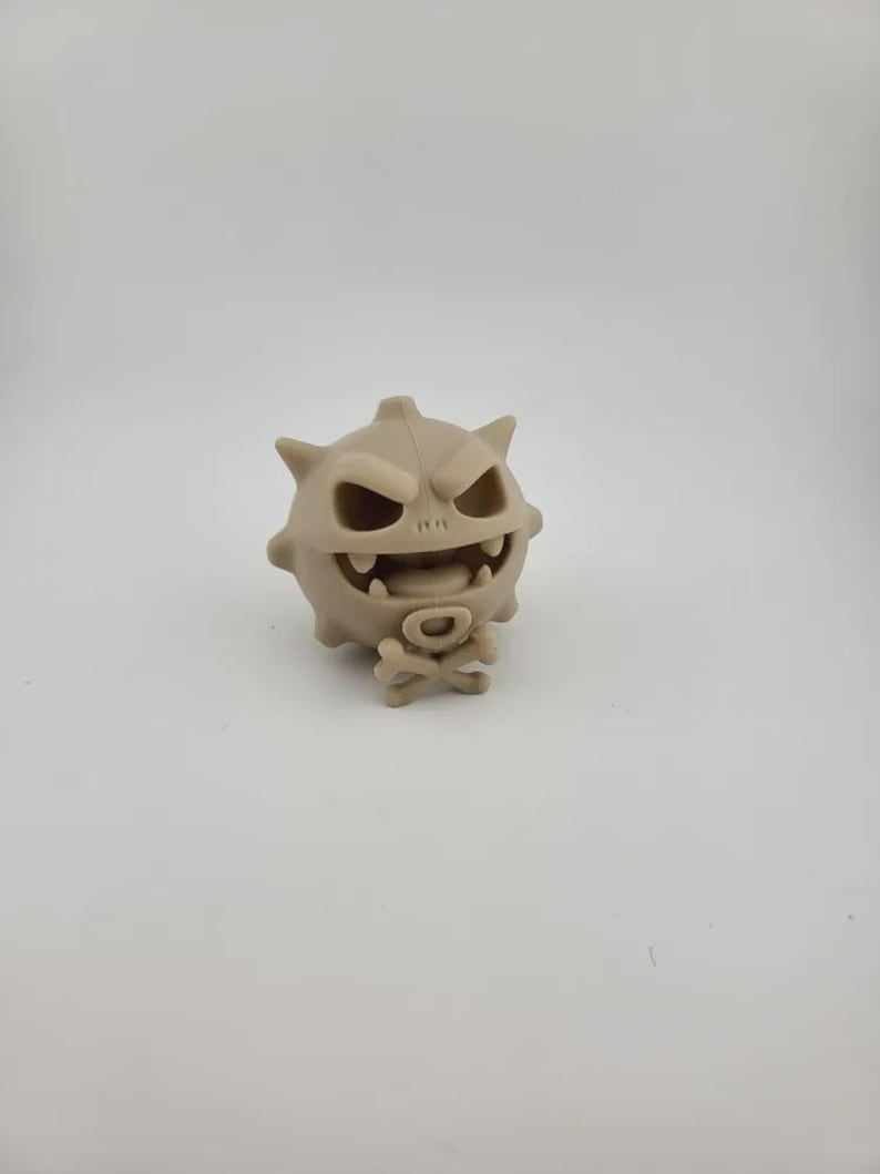 May include: A tan-colored, cartoonish figure with a spiky head, a wide, toothy grin, and a skull and crossbones emblem. The figure has a round body and a menacing expression, suggesting a playful, yet slightly spooky theme.
