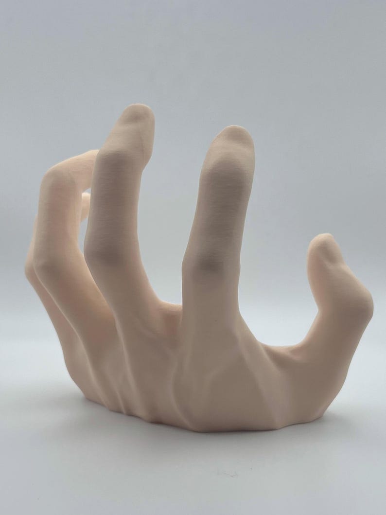 May include: A 3D printed hand sculpture in a light beige colour. The hand is posed with the fingers curled inwards, as if grasping something.