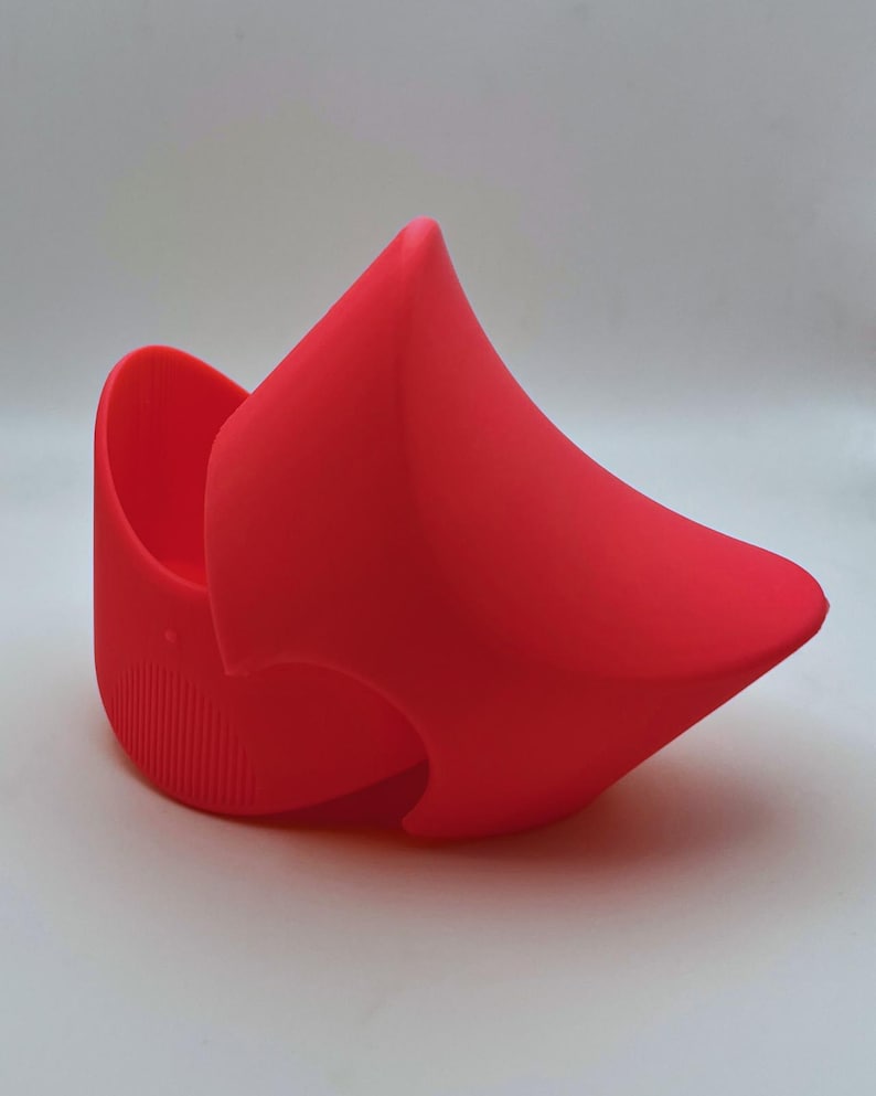 K&ouml;nnte beinhalten: Ein leuchtend roter Topfuntersetzer aus Silikon mit einem einzigartigen, geschwungenen Design. Der Halter hat eine abgerundete Basis mit vertikalen Rippen und eine spitze, abstrakte Form, die sich nach oben erstreckt. Die Gesamtform ist glatt und modern.