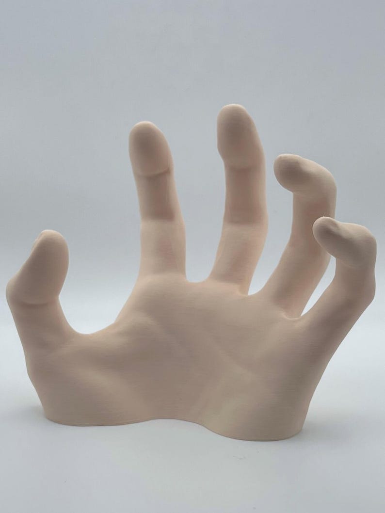 May include: A pale pink ceramic hand sculpture with an open palm and outstretched fingers. The hand is positioned as if reaching out or grasping.