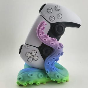 Puede incluir: Un mando de videojuegos blanco y negro está adornado con un diseño de tentáculo de pulpo colorido y degradado. El tentáculo hace la transición del rosa al azul y al verde, agregando una estética única al accesorio de juego.