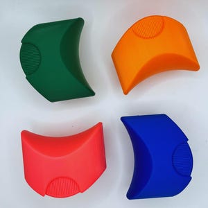 K&ouml;nnte beinhalten: Vier farbige K&uuml;chenhelfer aus Silikon in Gr&uuml;n, Orange, Rot und Blau. Jedes Werkzeug hat eine gebogene Form mit einem strukturierten, kreisf&ouml;rmigen Griff. Die Werkzeuge sind f&uuml;r den K&uuml;chengebrauch bestimmt und vor wei&szlig;em Hintergrund angeordnet.