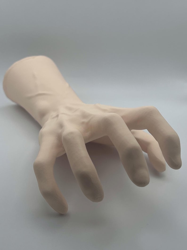 May include: A pale pink, realistic-looking hand model with all fingers extended and slightly curled. The hand is posed as if reaching out or grabbing something.