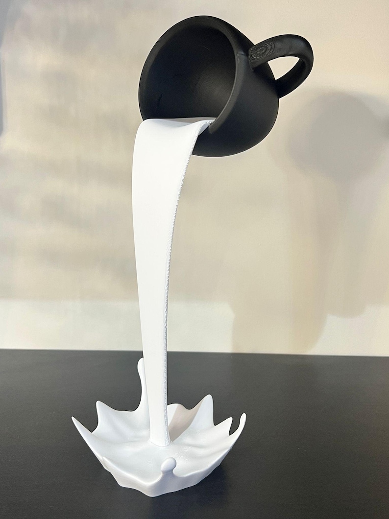 May include: A black ceramic cup pouring white liquid into a white ceramic splash. The cup is upside down and the liquid is frozen in mid-air.