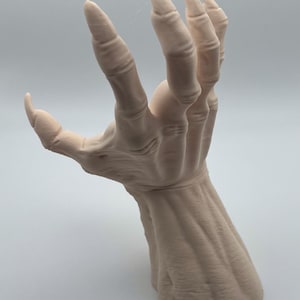 May include: A detailed, realistic sculpture of a pale, skeletal hand with long, sharp claws. The hand is posed in a grasping gesture, with the fingers extended and the palm facing outward. The sculpture is made of a smooth, white material and appears to be made of a durable, high-quality material.