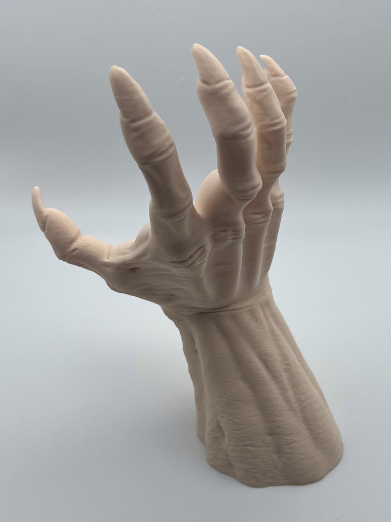 May include: A detailed, realistic sculpture of a pale, skeletal hand with long, sharp claws. The hand is posed in a grasping gesture, with the fingers extended and the palm facing outward. The sculpture is made of a smooth, white material and appears to be made of a durable, high-quality material.