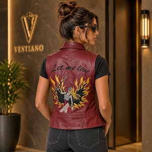 May include: A burgundy leather vest with the embroidered phrase "Let me live" on the back. The vest features a warrior graphic with yellow and black detailing. The sleeveless vest has a classic collar.
