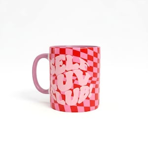 Może przedstawiać: Ceramiczny kubek z czerwono-różowym wzorem szachownicy. Kubek zawiera napis "SELF LUV CLUB!" w różowych literach bąbelkowych. Uchwyt jest w jednolitym różowym kolorze.
