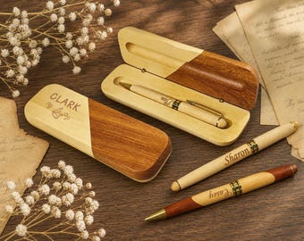 May include: Three wooden pens and two wooden cases with a two-tone light and dark wood finish. One case is open with a pen inside engraved with the name Elisa. The closed case is engraved with the name Clark. Two pens are engraved with Sharon and Casey.